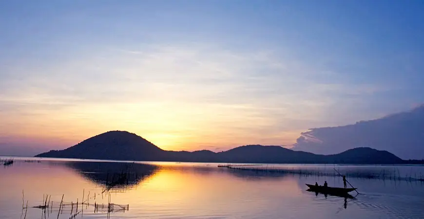 Tramonto su un lago asiatico con una barca di pescatori